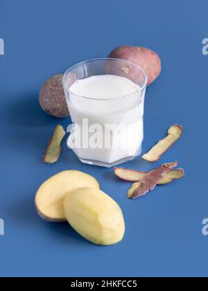 Un verre transparent avec du lait de pomme de terre végétale sur une table bleue près des tubercules de pomme de terre.Gros plan sur le lait sans lactose à base de plantes végétaliennes.Une alimentation saine et Un Banque D'Images