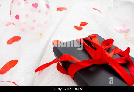 Boîte cadeau emballée et carte postale décorée d'un joli noeud rouge sur le lit.Saint-Valentin, anniversaire amour cadeau.Le concept de désherbage et de lune de miel.Amoureux Banque D'Images