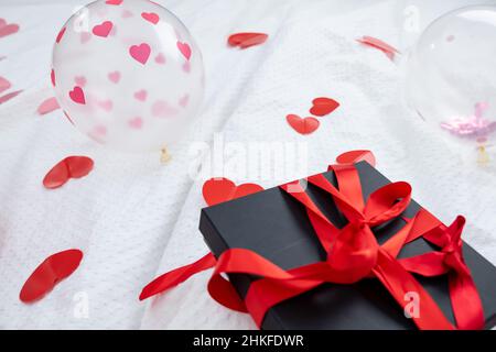 Boîte cadeau emballée et carte postale décorée d'un joli noeud rouge sur le lit.Saint-Valentin, anniversaire amour cadeau.Le concept de désherbage et de lune de miel.Amoureux Banque D'Images