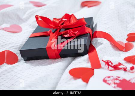 Boîte cadeau emballée et carte postale décorée d'un joli noeud rouge sur le lit.Saint-Valentin, anniversaire amour cadeau.Le concept de désherbage et de lune de miel.Amoureux Banque D'Images