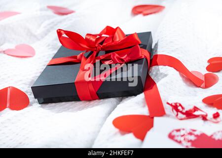 Boîte cadeau emballée et carte postale décorée d'un joli noeud rouge sur le lit.Saint-Valentin, anniversaire amour cadeau.Le concept de désherbage et de lune de miel.Amoureux Banque D'Images