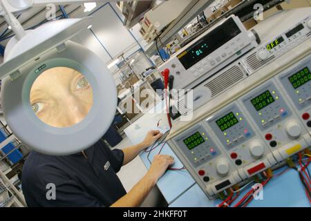 Technicien en laboratoire utilisant une grande loupe éclairée pour visualiser les composants électriques et les cartes de circuits imprimés. Banque D'Images