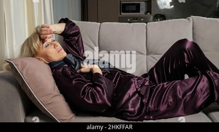 Une femme âgée est malade en pyjama et en foulard toussant Banque D'Images