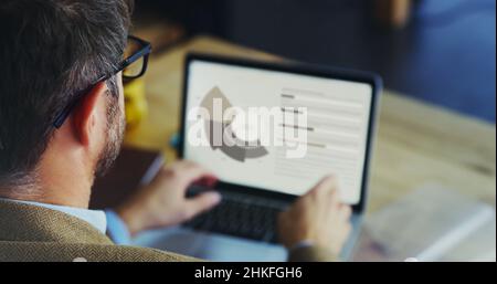 Examen des données.Vue arrière d'un homme d'affaires méconnu travaillant sur un ordinateur portable assis à son bureau. Banque D'Images