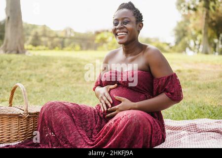 Young african pregnant woman touching her belly outdoor at city park - Focus on face Stock Photo