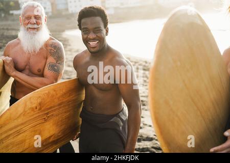 Amis surfeurs multigénérationnels s'amuser sur la plage après la session de surf - Focus sur le visage de l'homme africain Banque D'Images