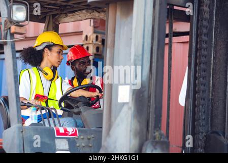 Deux hommes et femmes afro-américains travaillant en uniforme et avec un casque, sur un chariot élévateur à conteneur diesel, sur un quai commercial. Banque D'Images