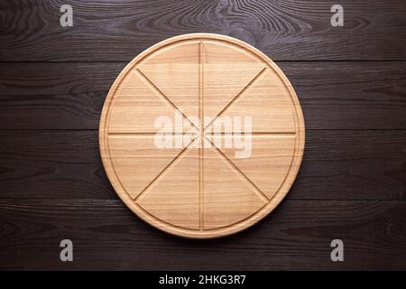 Planche à découper ronde à pizza avec rainures en tranches sur table en bois marron vue sur le dessus Banque D'Images