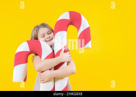 Une jeune fille adorable encadre deux énormes canes de bonbons sur fond jaune.Joyeux préchooler avec des bonbons entre les mains.Lollipop.Bonbons de Noël.Gros plan Banque D'Images