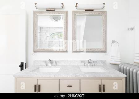 Une salle de bains avec un meuble-lavabo double couleur crème, comptoir en marbre, et des lumières suspendues au-dessus des miroirs. Banque D'Images