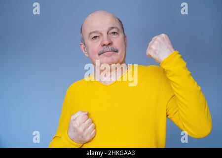 Homme d'âge moyen levant les armes, célébrant une victoire ou un succès.Studio tourné sur un mur bleu. Banque D'Images