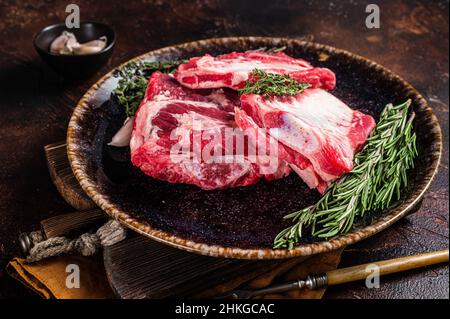 Côtelettes de veau cru non cuites sur une assiette rustique au romarin.Arrière-plan sombre.Vue de dessus Banque D'Images