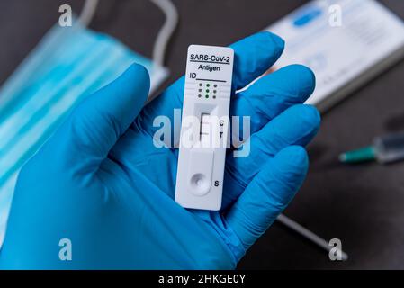 Une main portant un gant de protection est considérée en tenant un test Covid rapide, également appelé test d'antigène ou test de flux latéral, montrant un résultat positif dans un Banque D'Images