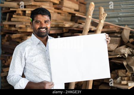 Joyeux souriant Carpenter avec panneau blanc regardant la caméra - concept des artisans promotion et la publicité pour les affaires locales Banque D'Images