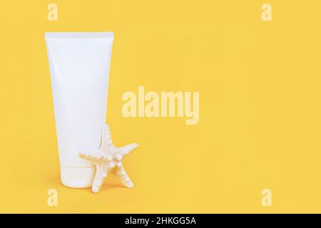 Tube cosmétique blanc vierge avec crème solaire, crème solaire pour le visage ou le corps et étoile de mer sur fond jaune. Concept soins de la peau en vacances d'été Mockup fron Banque D'Images