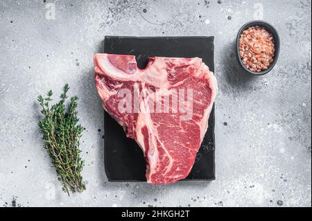 Steak de bœuf Wagyu vieilli et sec, non cuit, en T-bone sur un plateau de marbre au thym.Arrière-plan gris.Vue de dessus Banque D'Images