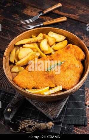 Schnitzel de weiner frits d'Autriche avec des quartiers de pommes de terre dans une assiette en bois.Arrière-plan en bois.Vue de dessus Banque D'Images