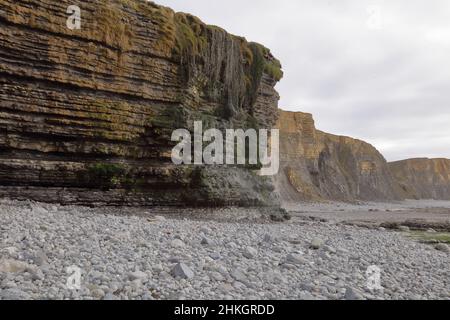 Vue vers le sud depuis la baie de Dunraven avec la chute d'eau Magic qui coule doucement sur le sommet de la falaise et sur le sable. Banque D'Images