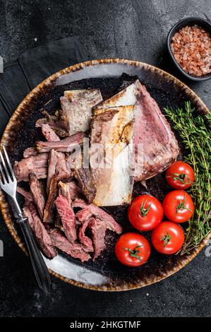 Côtelettes de bœuf fumées et grillées dans une assiette rustique aux herbes.Arrière-plan noir.Vue de dessus Banque D'Images