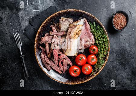 Côtelettes de bœuf fumées et grillées dans une assiette rustique aux herbes.Arrière-plan noir.Vue de dessus Banque D'Images
