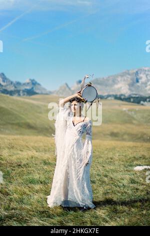 Fille avec un tambourin dans sa main se tient dans une vallée verte Banque D'Images