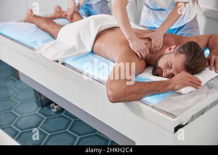 Un médecin attentif fait un massage de l'homme d'âge moyen et du dos avec un collègue en clinique Banque D'Images