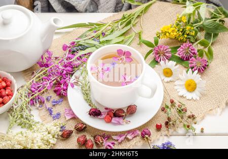 Tisane au rosehip, camomille et trèfle dans une tasse blanche sur une table blanche en bois avec des fleurs. Banque D'Images