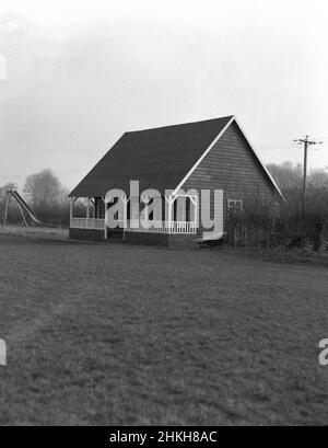 1950s, vue historique et extérieure d'un pavillon sportif traditionnel de l'époque construit avec un cadre en bois sur une base en brique et un toit en pente.D'un point de vue architectural, avec une véranda couverte ou une véranda à l'avant, ces types de bâtiments d'un étage situés en bordure des terrains de sport ont été vus dans de nombreux terrains de loisirs et de sport en Grande-Bretagne à l'heure actuelle, offrant des vestiaires pour les sports d'équipe tels que le cricket, le rugby et le football.À côté de ce pavillon récemment construit à Witney, Oxford, Angleterre, Royaume-Uni, une aire de jeu de chlldrens, avec toboggan de médaille. Banque D'Images