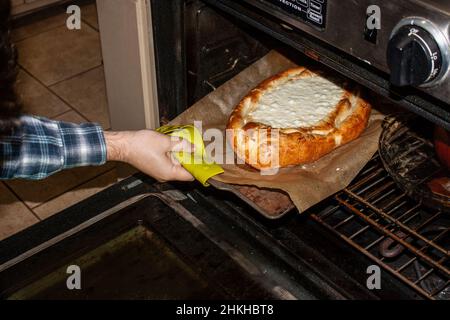 Retirez à la main le khachapuri géorgien du four avec du pain bruni et du fromage bouillant Banque D'Images