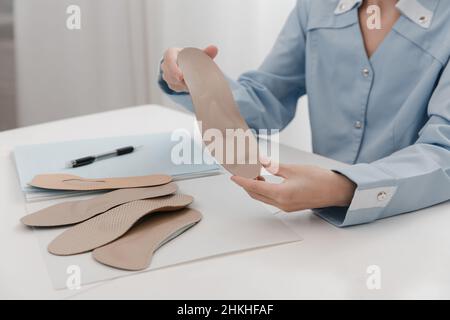 Médecin tenant une semelle intérieure tout en étant assis à une table.L'orthopédiste teste l'appareil médical.Semelles intérieures orthopédiques.Soins des pieds.Correction des pieds plats Banque D'Images