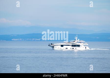 Un grand bateau à moteur touristique navigue sur une mer Méditerranée calme contre une petite ville côtière près de grandes montagnes forestières le matin ensoleillé Banque D'Images