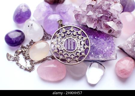 Pendentif rond argenté et chaîne sur des pierres semi-précieuses.Bijoux en argent et druze d'améthyste, cristal de roche et quartz rose sur une table blanche Banque D'Images