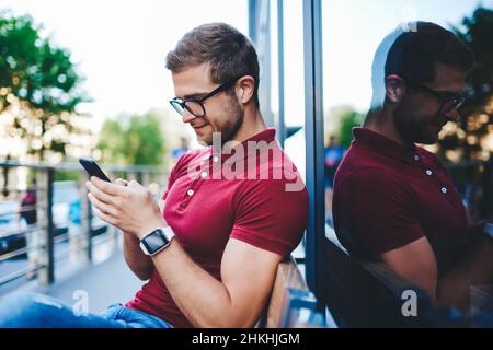 Messagerie texte gaie non rasée sur un téléphone intelligent, assis sur le trottoir Banque D'Images