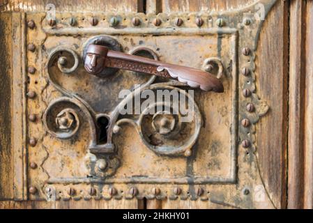 Gros plan d'une ancienne porte en bois décorée de bois sculpté avec des garnitures corrodées et rouillées, éléments d'une serrure métallique décorative, poignée de porte Banque D'Images