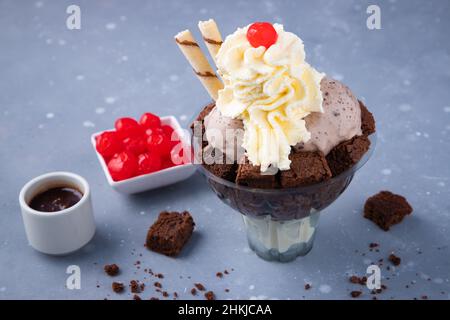 Glace savoureuse avec des brownies et de la crème fouettée sur une table grise Banque D'Images