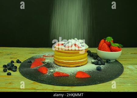 Crêpes aux baies de fruits sur fond noir.Crêpes fraîches.Bleuets, fraises sur crêpes.Saupoudrer le sucre glace sur les crêpes.Ardoise et Banque D'Images