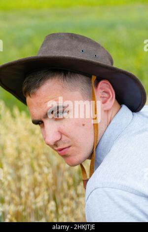 Homme en chapeau.Portrait de fermier avec du blé d'or et de l'herbe verte en arrière-plan.Jeune homme portant un chapeau de cow-boy sur le terrain.Gros plan.Bonne jeune personne. Banque D'Images
