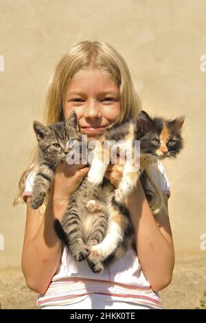 Chat domestique, chat maison (Felis silvestris F. catus), petite fille blonde tenant heureusement deux chaton dans ses mains Banque D'Images