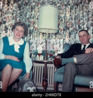 Un couple d'âge moyen pose devant des rideaux laids dans une maison MCM, 1963. Banque D'Images