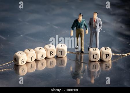 Modèle miniature d'hommes d'affaires et cubes en bois avec inscription de démarrage sur un fil sur une table réfléchissante. Banque D'Images