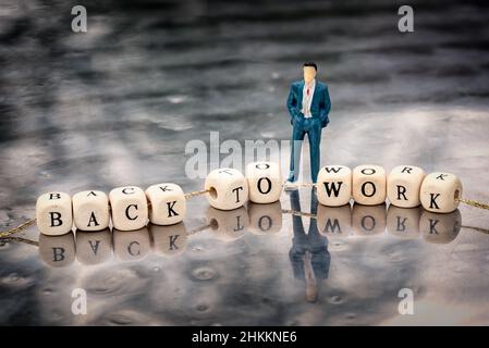 Modèle miniature d'homme et cubes en bois avec inscription dos au travail accroché à un fil sur une table réfléchissante. Banque D'Images