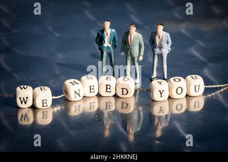 Modèle miniature d'hommes d'affaires et cubes en bois avec nous avons besoin de vous inscription strung sur un fil sur table réfléchissante.Le concept d'entreprise de recrutement. Banque D'Images