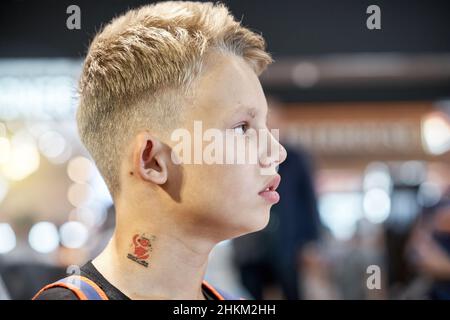 Un adolescent aux cheveux blonds ennuyé avec une expression faciale sérieuse se trouve dans la salle d'attente de l'aéroport contre une foule floue de très près Banque D'Images