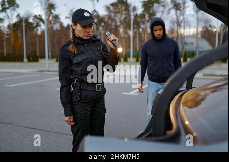 Femme policier inspectant la voiture avec une lampe de poche Banque D'Images