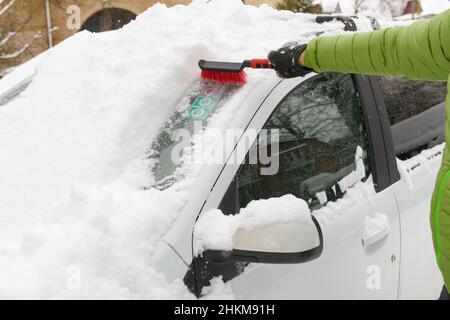 Homme nettoyant sa voiture en hiver, enlevant la neige profonde de la fenêtre Banque D'Images