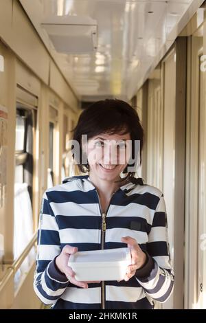 Une femme souriante descend le couloir du train avec un paquet de nouilles instantanées certifiées. Banque D'Images