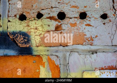Ancienne peinture colorée orange bleu noir avec des fissures sur le mur de brique rouge comme fond, texture, foyer sélectif Banque D'Images
