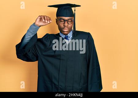 Jeune afro-américain portant une casquette de remise des diplômes et une robe de cérémonie qui s'étire, fatigué et détendu, endormi et bâilling tôt le matin Banque D'Images