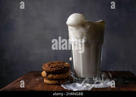 Éclaboussures de lait dans un verre et biscuits aux pépites de chocolat sur une table en bois Banque D'Images