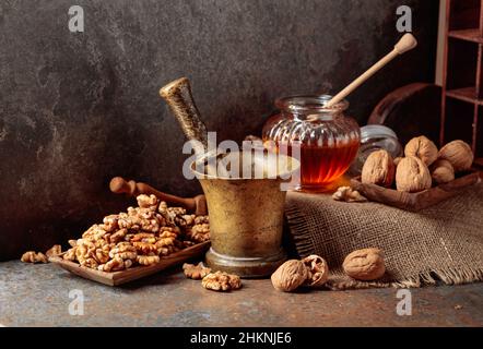 Noix, vieux mortier de laiton et miel sur une table de cuisine. Banque D'Images